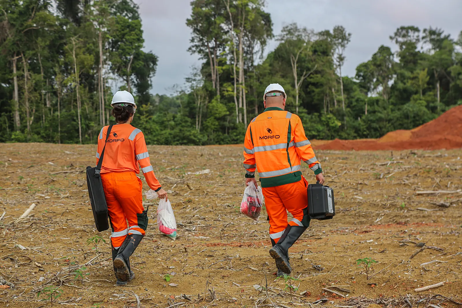 Dois agentes de campo da MORFO atravessando a frente exposta pós-bauxita em Paragominas, com o kit de amostragem na mão